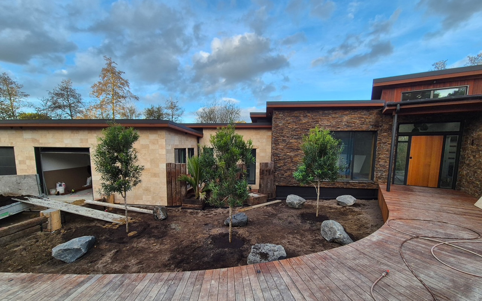 Modern house exterior with a landscaped garden area and wooden deck and showcasing Ewekuri, Wharangi & Nikau Trees